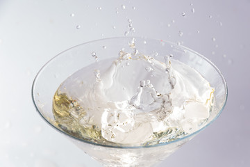 A glass with vermouth and a piece of ice thrown at it. splash and splash of drink