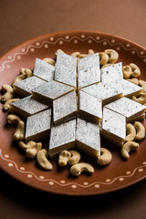 Kaju Katli is a Diamond shape Indian sweet made using cashew sugar and mava, served in a plate or bowl over moody background. selective focus