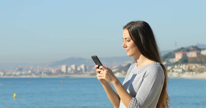 Side view portrait of a serious woman texting on a smart phone on the beach