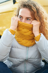Portrait of young attractive redhead curly girl siting front of yellow van and holding her yellow scarf