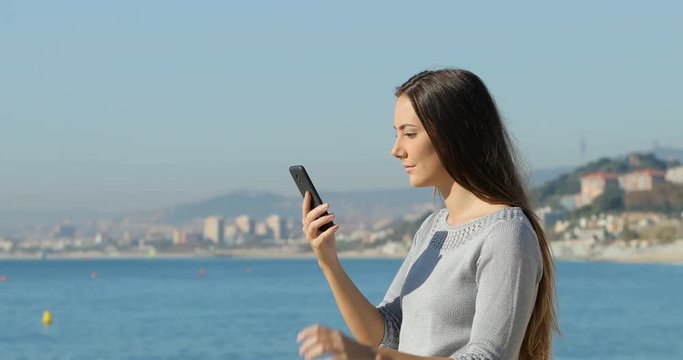 Side view portrait of a surprised woman finding exciting content in a smart phone on the beach