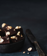 Schokoladen-Haselnuss-Fudge in dunkler Schale auf dunklem Untergrund mit viel freiraum für text bei tageslicht von vorne fotografiert