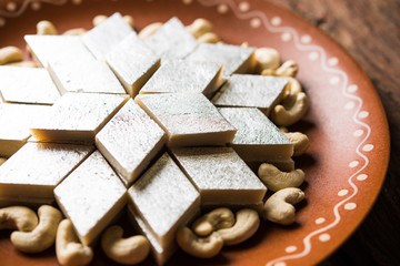 Kaju Katli is a Diamond shape Indian sweet made using cashew sugar and mava, served in a plate or bowl over moody background. selective focus