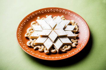 Kaju Katli is a Diamond shape Indian sweet made using cashew sugar and mava, served in a plate or bowl over moody background. selective focus