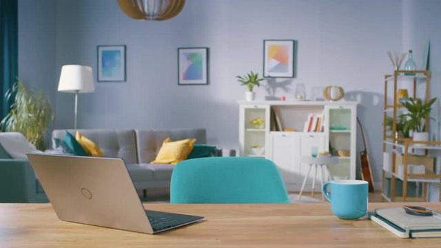 Zoom In Shot of the Stylish Interior of the Living Room with Wooden Working Desk with Laptop, Stylish Chairs, Sofa. Tastefully Colorful Furniture with Serene Tones, Pleasant Art on the Walls.