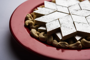 Kaju Katli is a Diamond shape Indian sweet made using cashew sugar and mava, served in a plate or bowl over moody background. selective focus