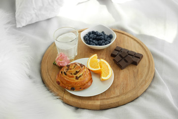 Wooden board with delicious breakfast on bed
