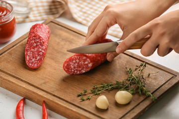 Woman cutting delicious smoked sausage on wooden board