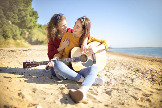 Mother and daughter singing and playing guitar at the beach