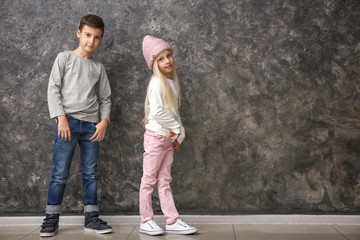 Cute boy and girl in fashionable clothes near grey wall