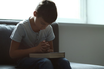 Little boy with Bible praying at home