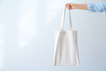 Female hand with eco bag on light background