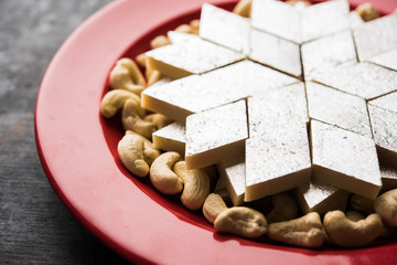 Kaju Katli is a Diamond shape Indian sweet made using cashew sugar and mava, served in a plate or bowl over moody background. selective focus