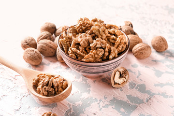 Bowl and spoon with tasty walnuts on color table