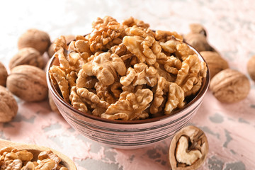 Bowl with tasty walnuts on color table