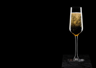Elegant glass of yellow champagne with bubbles on black marble board on black background. Space for text