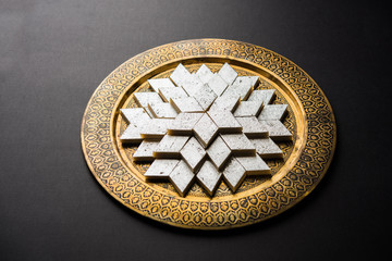 Kaju Katli is a Diamond shape Indian sweet made using cashew sugar and mava, served in a plate or bowl over moody background. selective focus