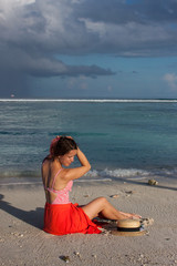 young woman with straw boater hat, red long skirt posing on Indian ocean beach on Maldives