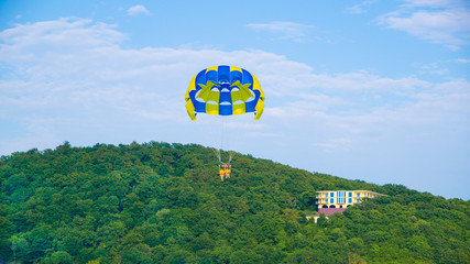 Parachute water fun. Flight on a parachute on the black sea over the trees at the resort. Beautiful blue and yellow parachute.