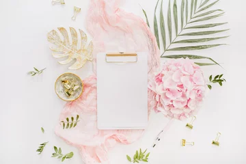 Rolgordijnen Blank paper clipboard, pink hydrangea flowers bouquet, tropical palm leaf, pastel blanket, monstera leaf plate and accessories on white background. Flat lay © Floral Deco