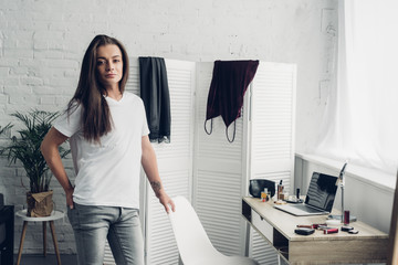 young transgender woman standing near workplace and looking at camera at home