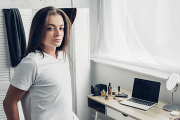 close-up portrait of young transgender woman standing near workplace and looking at camera at home