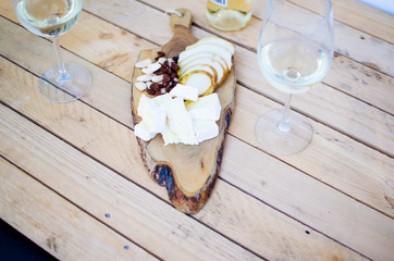 wooden slats table with bottle and glasses of white wine and snacks such as cheese, fruit and nuts