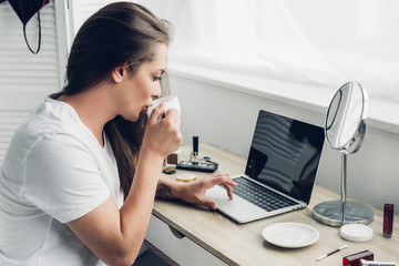 young transgender freelancer woman drinking coffee while working with laptop  at home