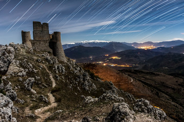 Fototapeta premium Star trail Rocca Calascio Fortress with moon Light Time, with Shadow - A Medieval Castle Built over the Peak of Mountain in Abruzzo - Italy, Corno Grande background