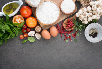 Italian food background, with tomatoes, basil, mushrooms, olives, olive oil, garlic, peppercorns, chilli, eggs, flour and oregano. Slate background.
