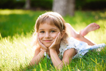 Naklejka na ściany i meble Cute little girl lies on grass in summer park