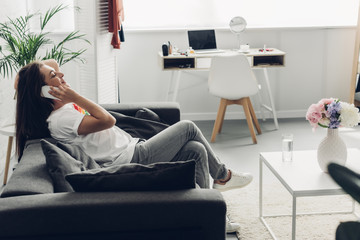 side view of smiling young transgender woman talking by phone on couch at home