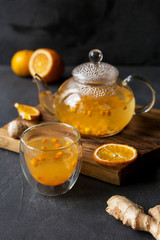 Sea buck thorn tea in glass teapot with glass cup, orange and ginger near on black background