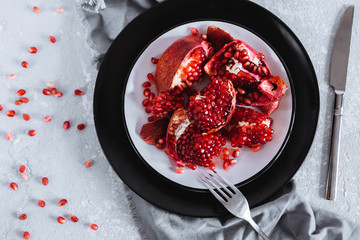 Juicy red pomegranate slices on a plate on a gray background, top view
