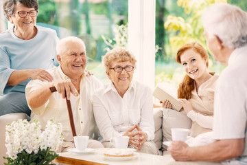 Happy elderly people drinking tea in the common room of nursing house