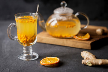 Sea buck thorn tea in glass teapot with glass cup and spoon, orange and ginger near on black background