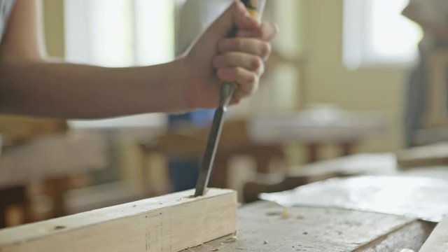 Close up view of man using hammer with chisel at woodworking workshop