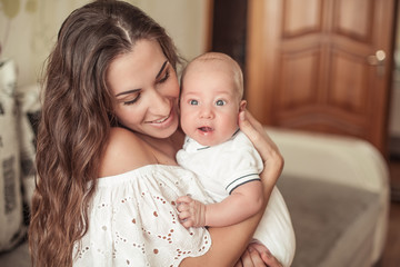 Beautiful young mother holds the baby in her arms. Mom holds the baby's legs in her hands for 3 months. Love. Motherhood. Happiness. House. Cozy.
