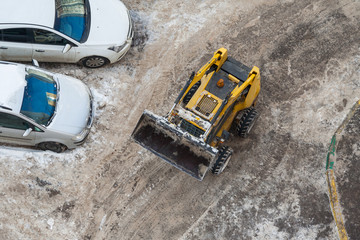 Top view of a snow-removing machine and a parked cars on a dirty road