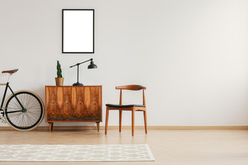 Stylish chair next to retro cabinet and vintage bike in scandinavian minimal interior with mockup...