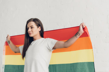 transgender man holding pride flag in front of white brick wall