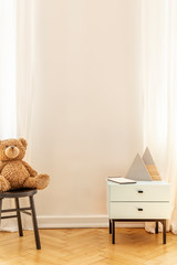 Real photo of an empty wall in a kid room interior with a teddy bear and cabinet with decorative triangles © Photographee.eu