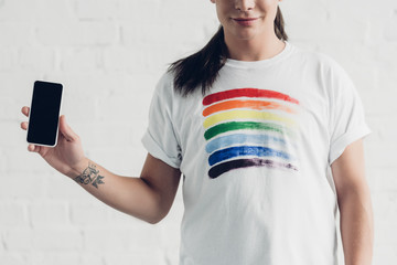 cropped shot of young transgender man in white t-shirt with pride flag holding smartphone with...