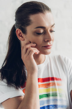 close-up portrait of young transgender man in white t-shirt with pride flag in front of white brick wall