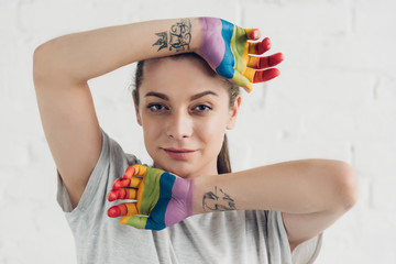 young transgender man with hands painted in colors of pride flag in front of white brick wall