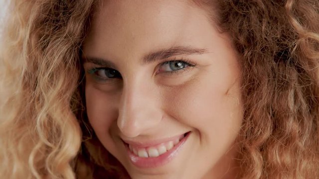 panned closeup video green eyed model with blonde curly hair watching at camera and smiling