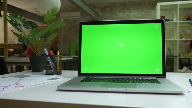Shooting of laptop on the table, green screen showing, office modern room, indoor