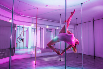 Strong but graceful. Strong but graceful pole dancer training hard in big and light studio with mirror - obrazy, fototapety, plakaty