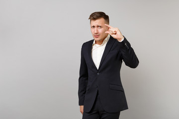 Concerned young business man in classic black suit, shirt gesturing demonstrating size with copy space isolated on grey wall background. Achievement career wealth business concept. Advertising area.