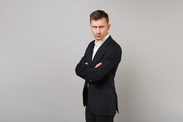 Side view of serious young business man in classic black suit and shirt holding hands folded isolated on grey wall background in studio. Achievement career wealth business concept. Mock up copy space.